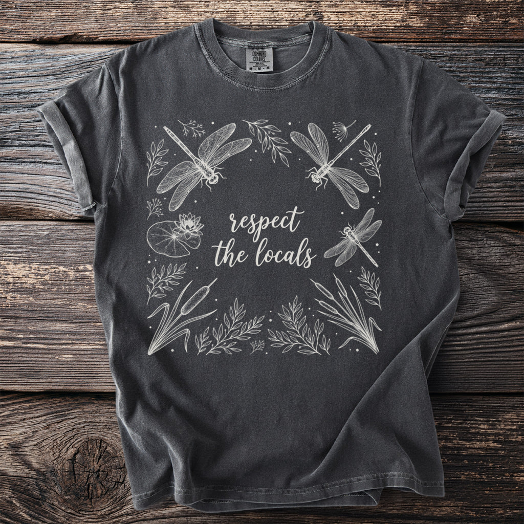 Dark gray t-shirt with white line art of dragonflies, water lilies, and reeds. "respect the locals" is written in script.