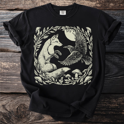 Black t-shirt with a cream linocut art of a fox and raven with moon and mushrooms.