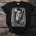 Black t-shirt with a cream-colored linocut-style print of a witch stirring a cauldron in a forest.