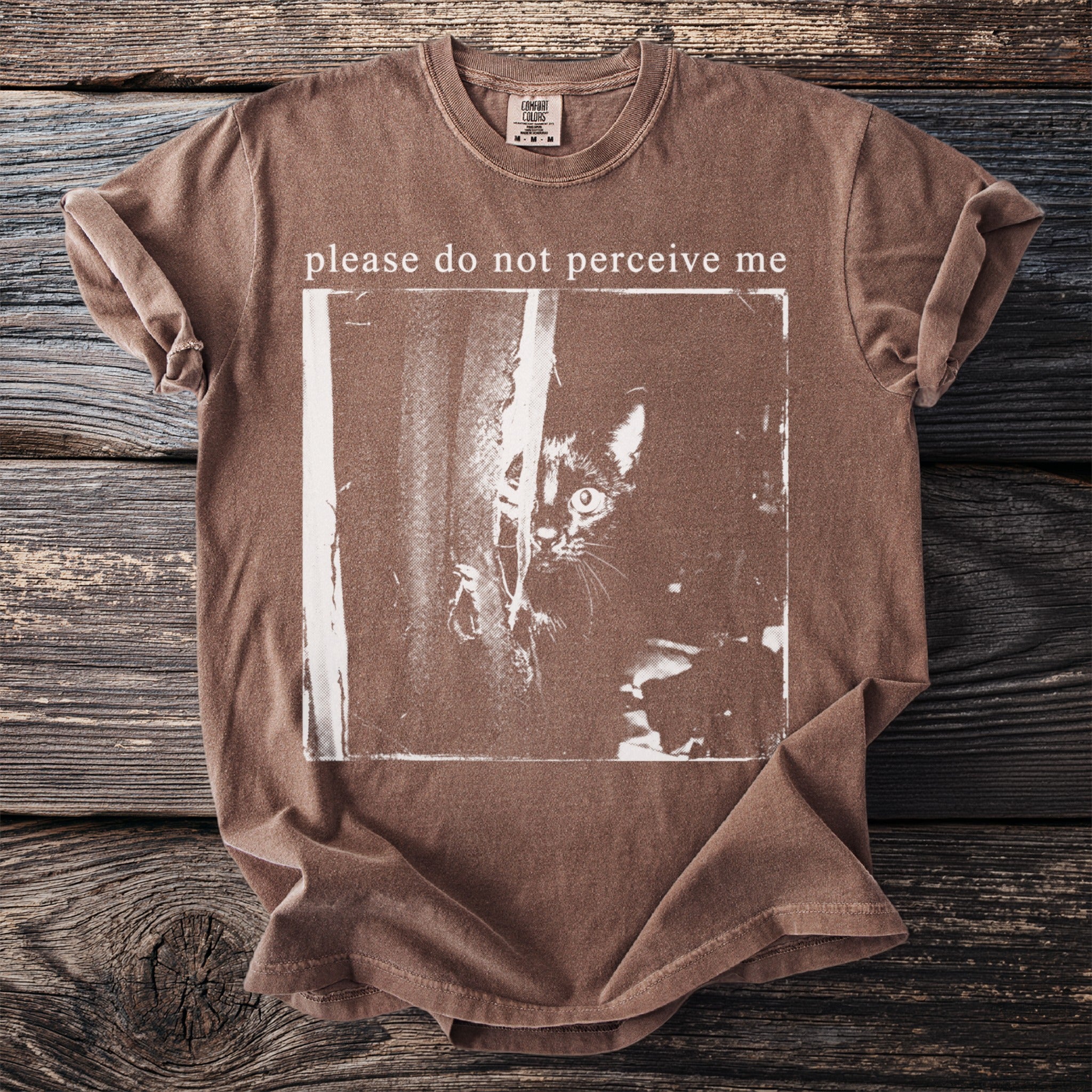 Brown t-shirt with "please do not perceive me" text and black cat graphic.