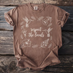 Brown t-shirt with white outline of hummingbirds, flowers, and text "respect the locals".