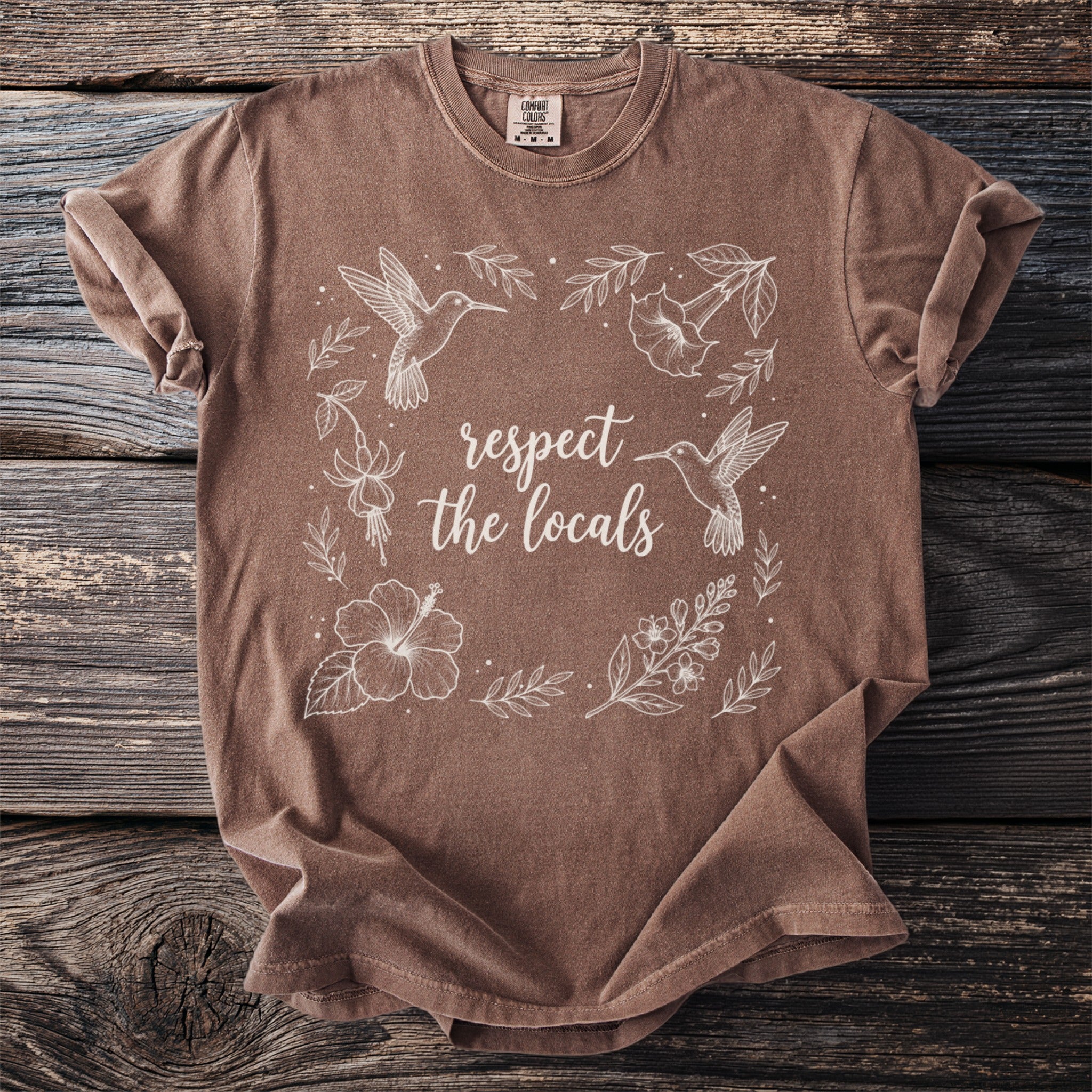 Brown t-shirt with white outline of hummingbirds, flowers, and text "respect the locals".
