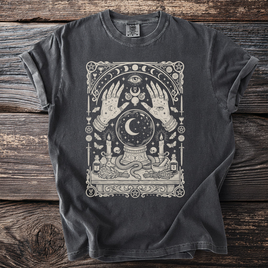 Dark t-shirt with a cream-colored mystical design featuring hands, crystal ball, snake, and candles.