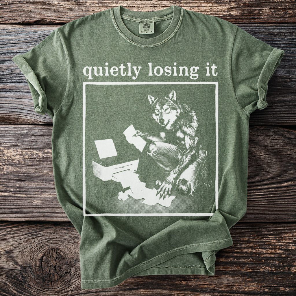 Green t-shirt with white graphic of wolf by printer, reading "quietly losing it".