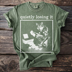 Green t-shirt with white graphic of wolf by printer, reading "quietly losing it".