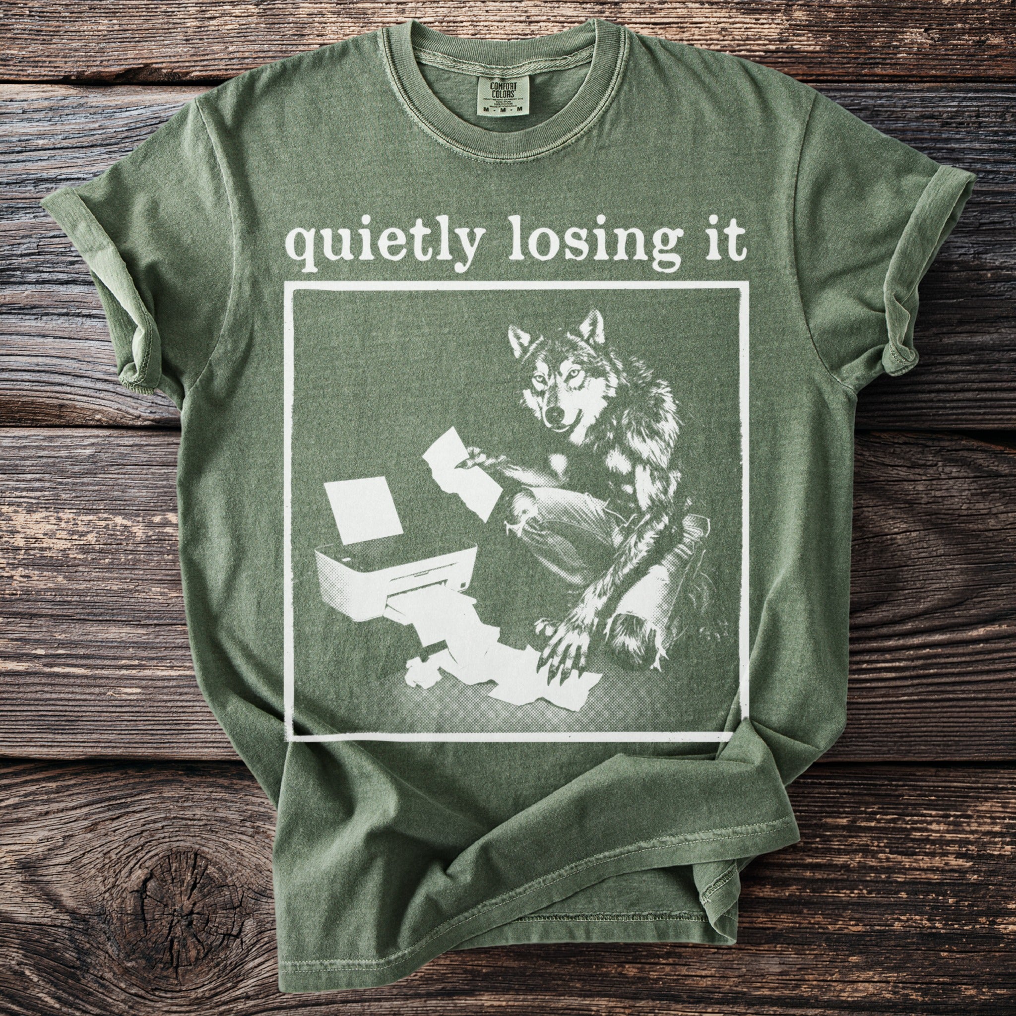 Green t-shirt with white graphic of wolf by printer, reading "quietly losing it".
