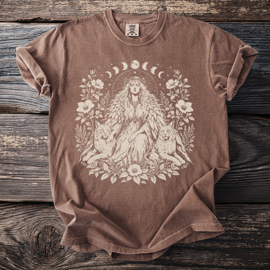 Brown Comfort Colors t-shirt with a cream graphic of a woman, two lynxes, and floral elements.