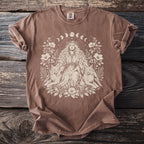 Brown Comfort Colors t-shirt with a cream graphic of a woman, two lynxes, and floral elements.