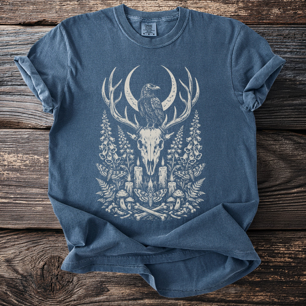 Blue t-shirt with white graphic of deer skull, raven, crescent moon, and botanical elements.