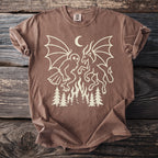 Brown t-shirt with cream linework of a creature and a goat-like figure over a fire and trees.
