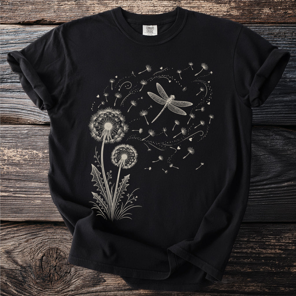 Black t-shirt with a dandelion and dragonfly graphic and scattered seeds.