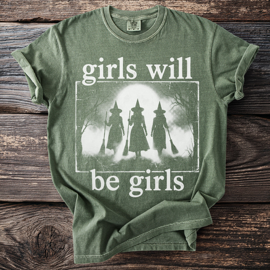 Green t-shirt with white distressed graphic of three witches and text "girls will be girls".
