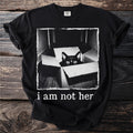 Black t-shirt with a black cat peeking out of a box and text "i am not her".