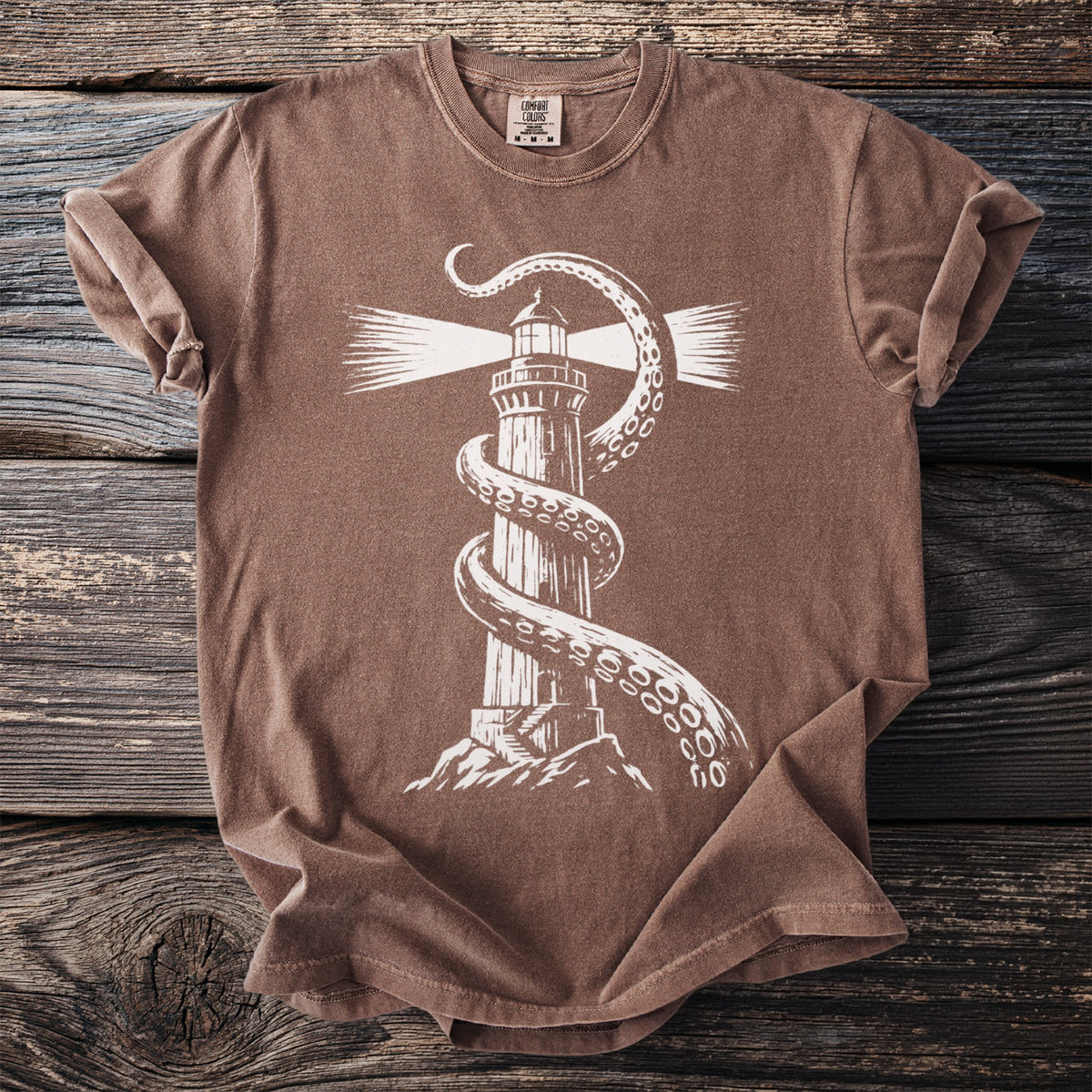 Brown t-shirt with a white graphic of a lighthouse wrapped by octopus tentacles.