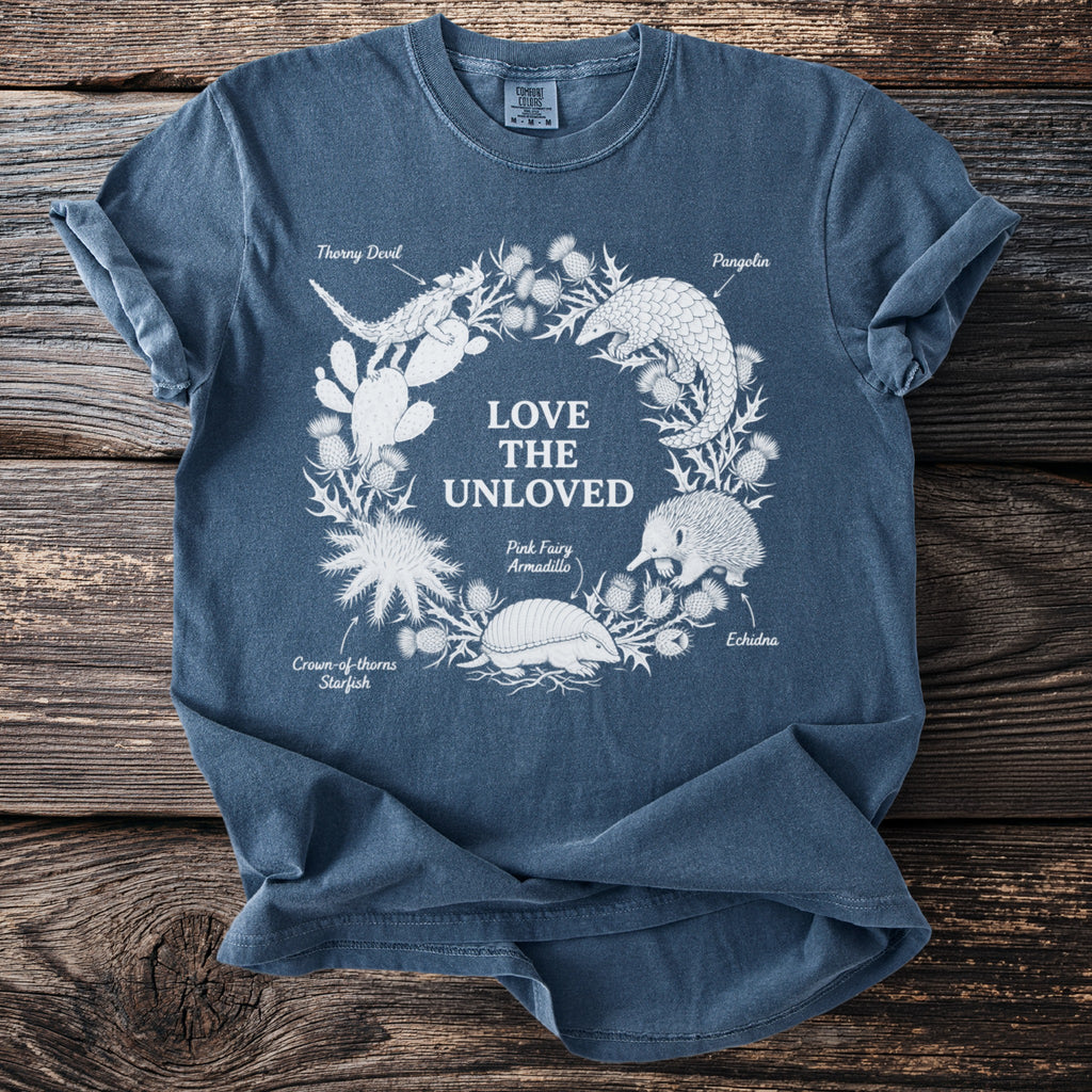 Front of blue t-shirt with "Love the Unloved" surrounded by illustrated animals and text labels.