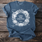 Front of blue t-shirt with "Love the Unloved" surrounded by illustrated animals and text labels.