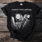 Black t-shirt with "Support Local Goblins" text and two possums on a fence.