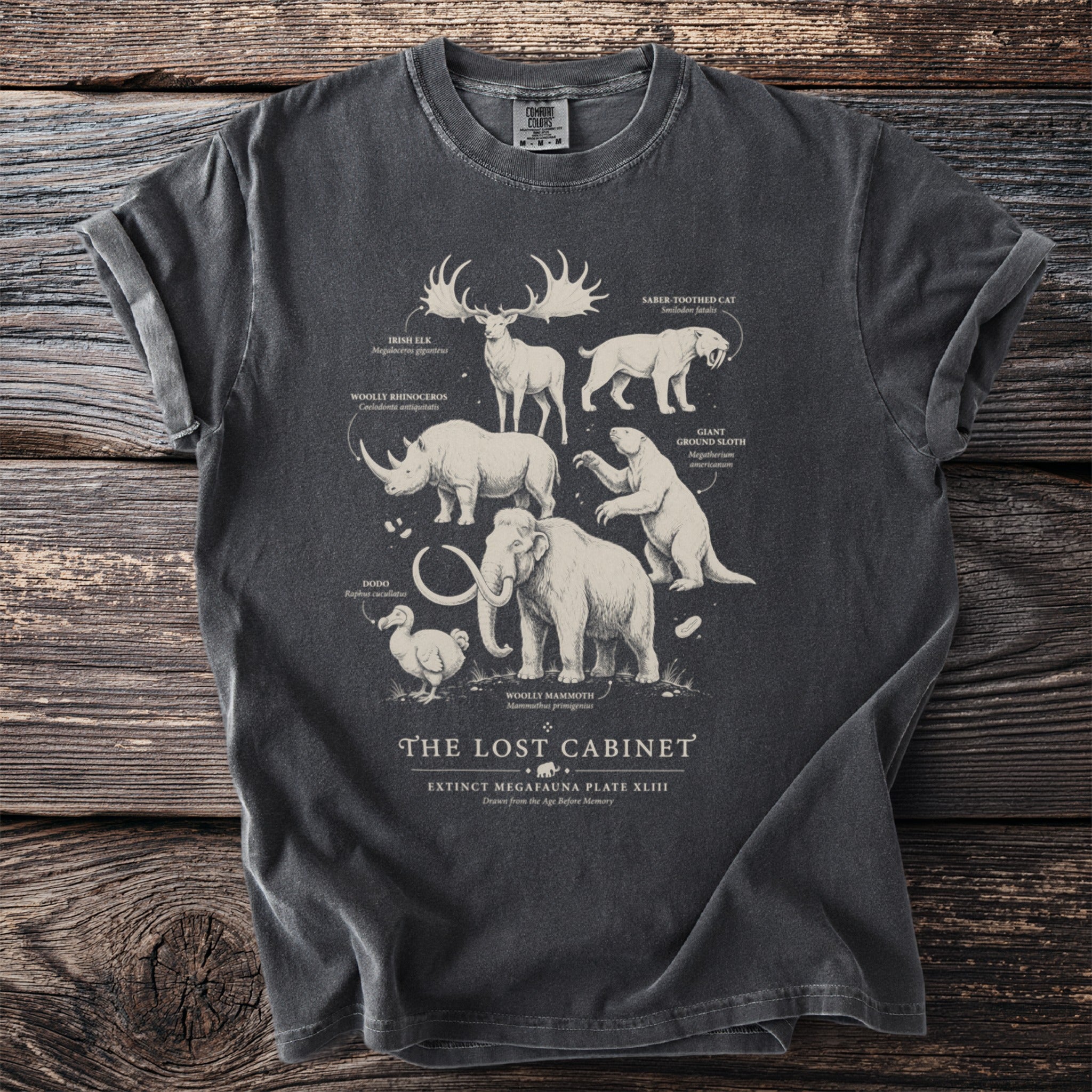 Grey t-shirt featuring extinct megafauna illustrations: Irish Elk, Woolly Rhino, Dodo, Saber-toothed Cat, Giant Ground Sloth, Woolly Mammoth.