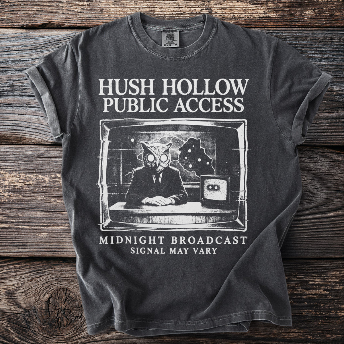 Dark gray t-shirt with "Hush Hollow Public Access" and owl news anchor graphic.
