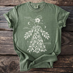Green t-shirt with white botanical illustration of a witch and labeled plants.