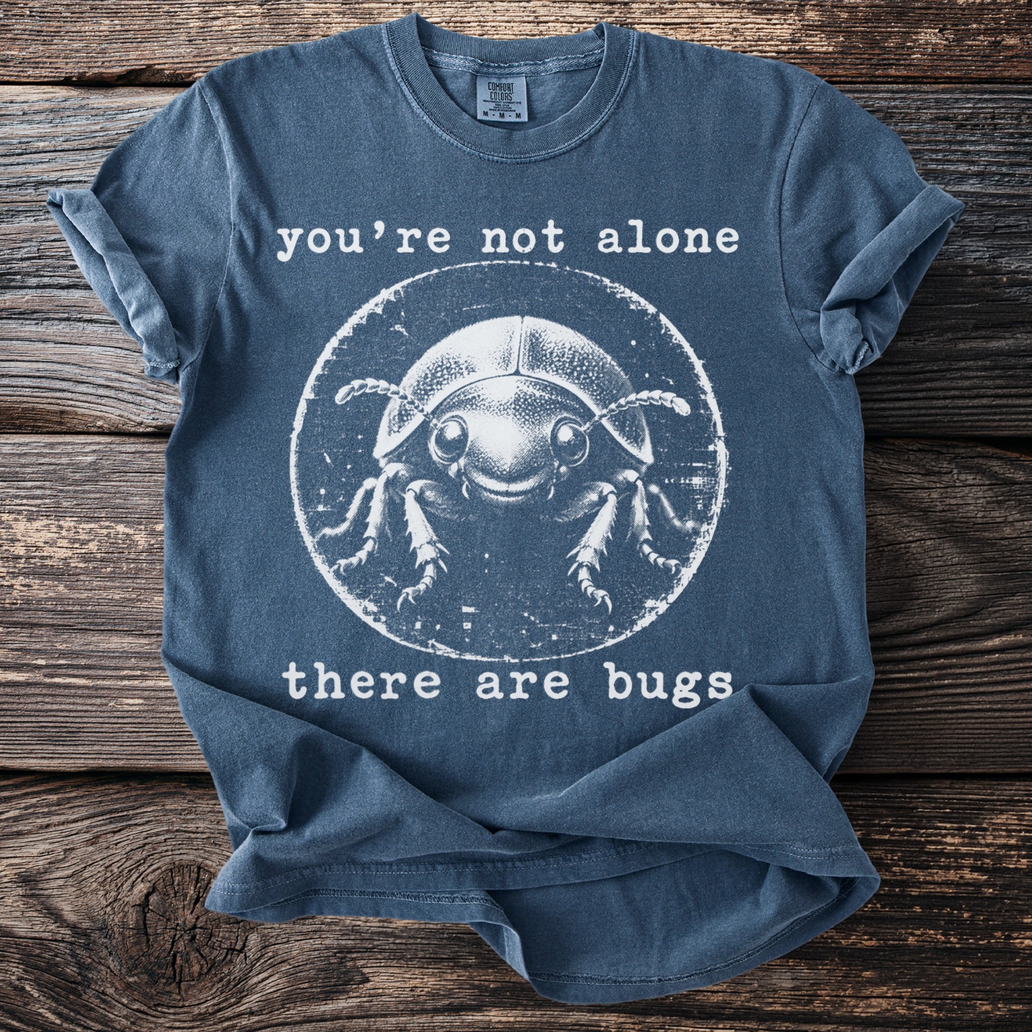 Blue t-shirt with graphic of a smiling beetle and text "you're not alone there are bugs".