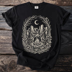 Black t-shirt with a tondo graphic of figures in robes dancing around a campfire under a moon.