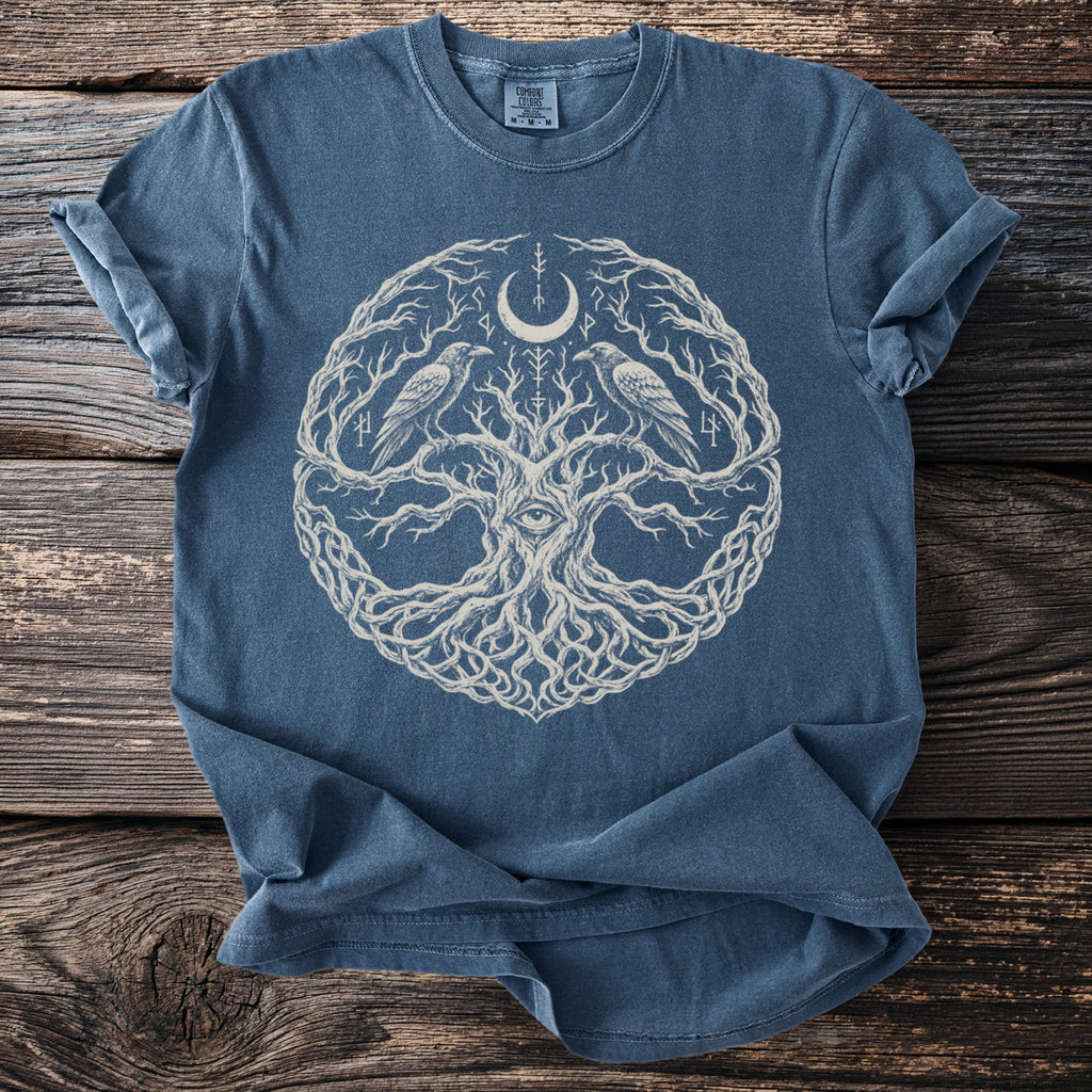 Blue t-shirt featuring an illustration of a tree with an eye, ravens, crescent moon, and runes.