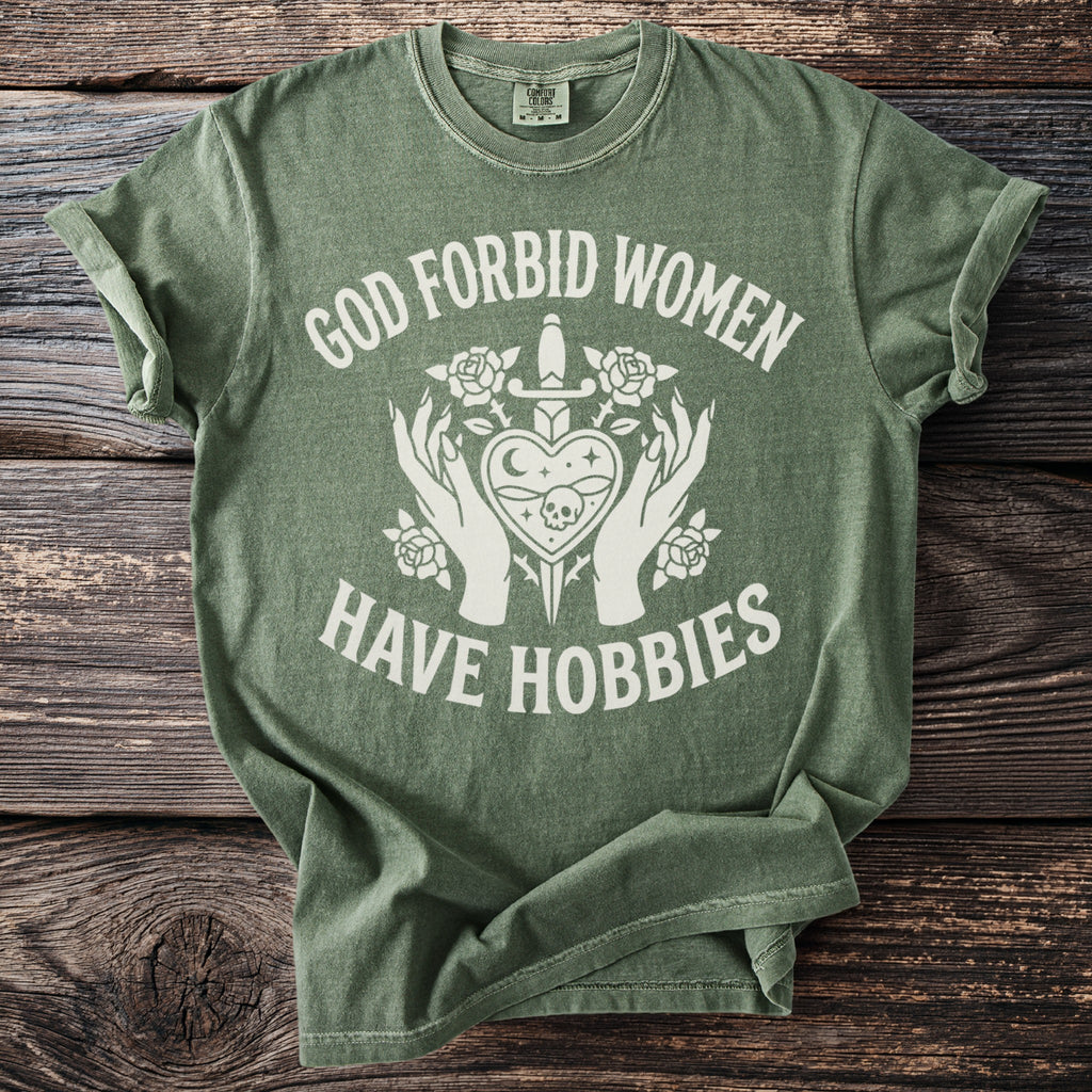 Green t-shirt with white text "God forbid women have hobbies" and graphic.