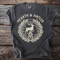 Dark gray t-shirt with "HEARTH & ANTLER" above a deer and campfire emblem.