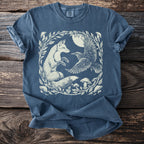 Blue t-shirt with a white illustration of a fox, raven, and mushrooms in a circular leafy frame.