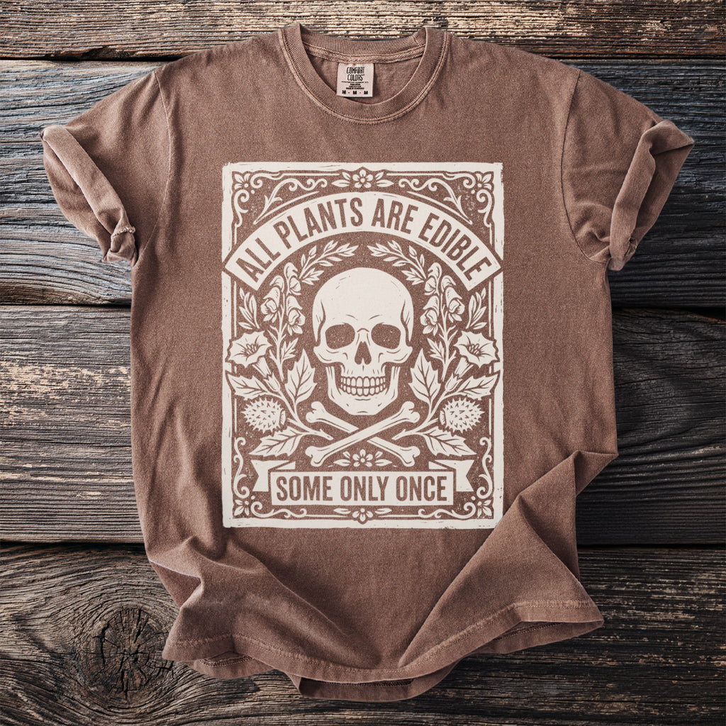 Brown t-shirt with skull, bones, plants, and text "ALL PLANTS ARE EDIBLE SOME ONLY ONCE".