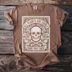 Brown t-shirt with skull, bones, plants, and text "ALL PLANTS ARE EDIBLE SOME ONLY ONCE".