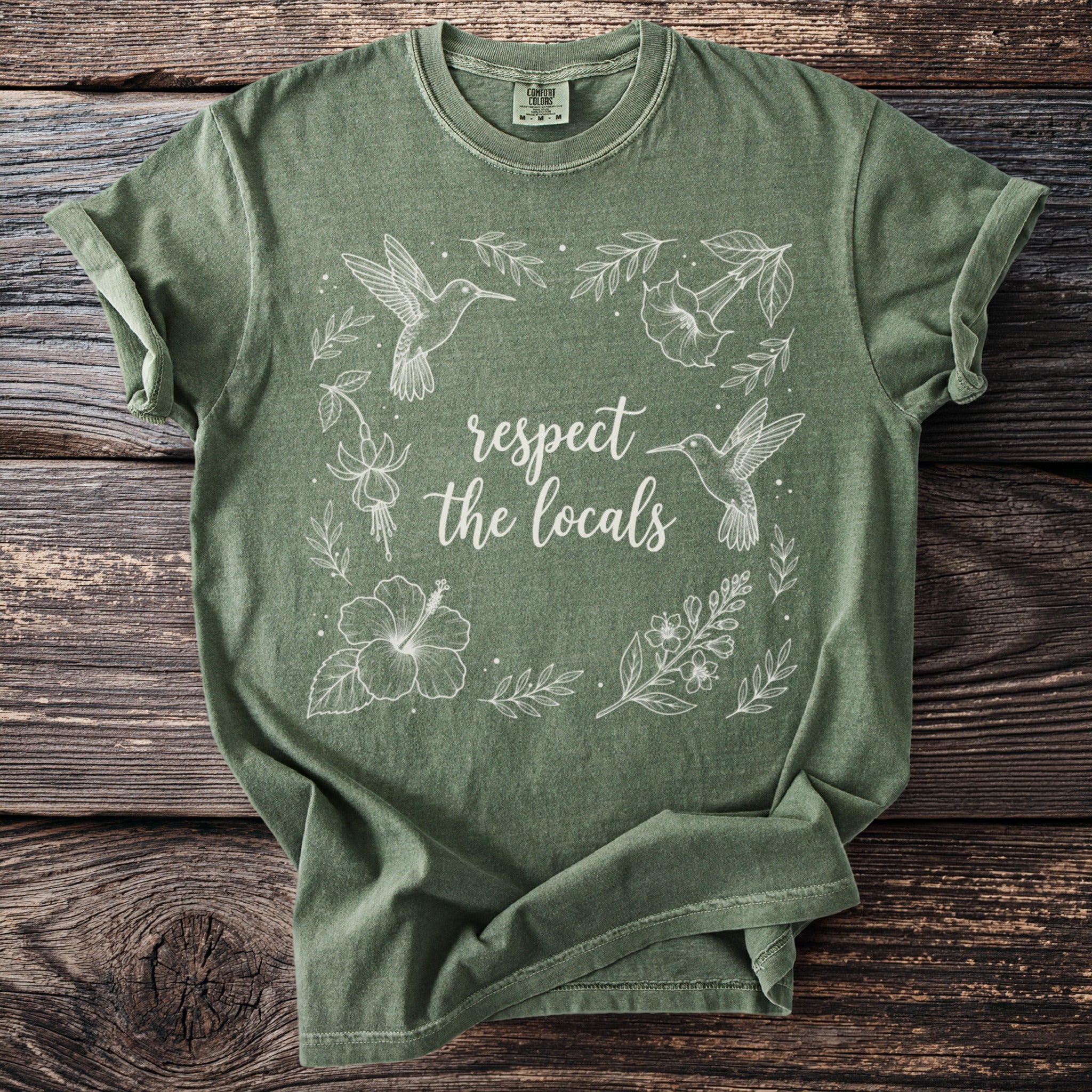 Green t-shirt with white line art of hummingbirds, flowers, and text "respect the locals".