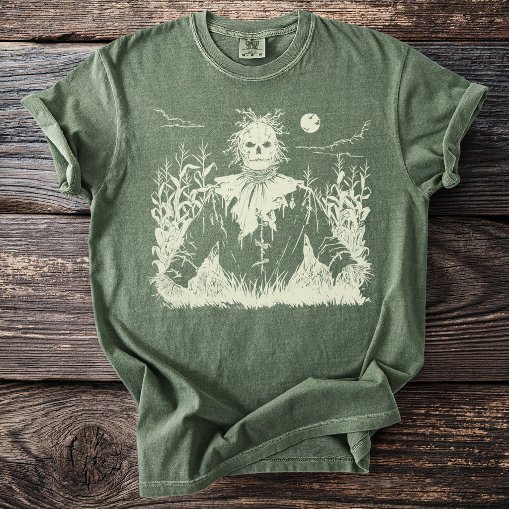 Green t-shirt with a cream scarecrow graphic in a cornfield at night.