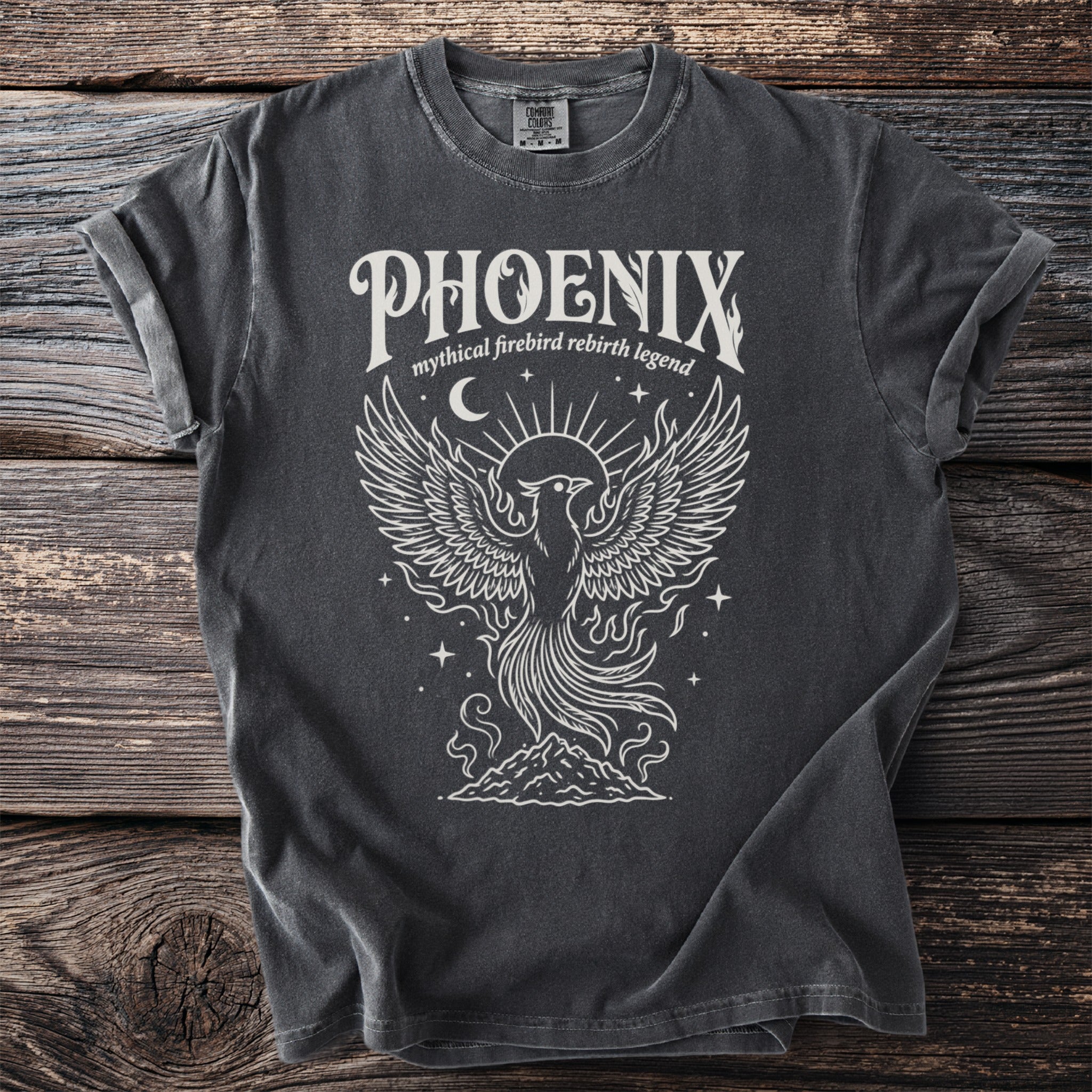 Dark grey t-shirt with white graphic of a phoenix rising from mountains, text "PHOENIX mythical firebird rebirth legend".