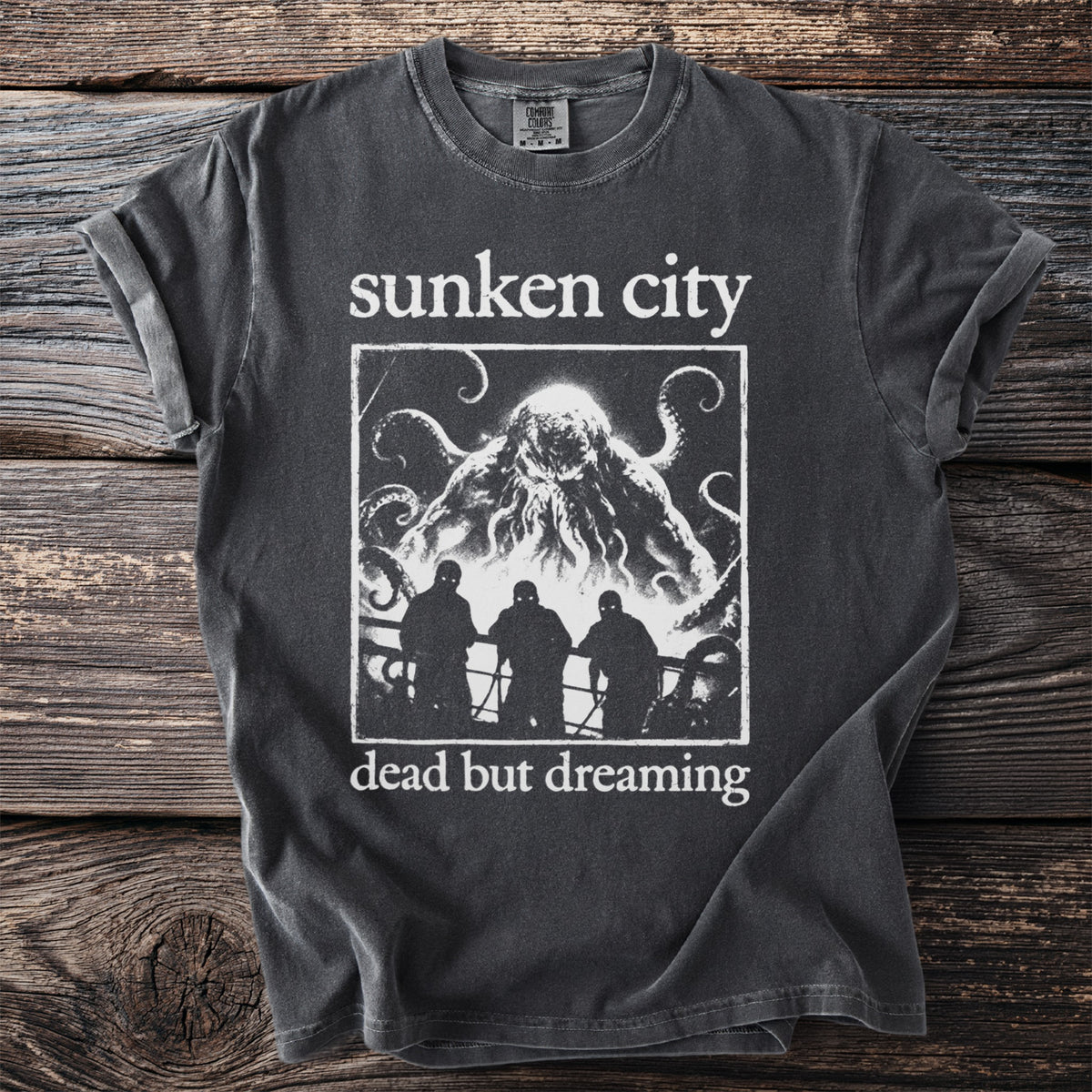 Dark grey t-shirt with white text "sunken city" and a kraken above three figures.