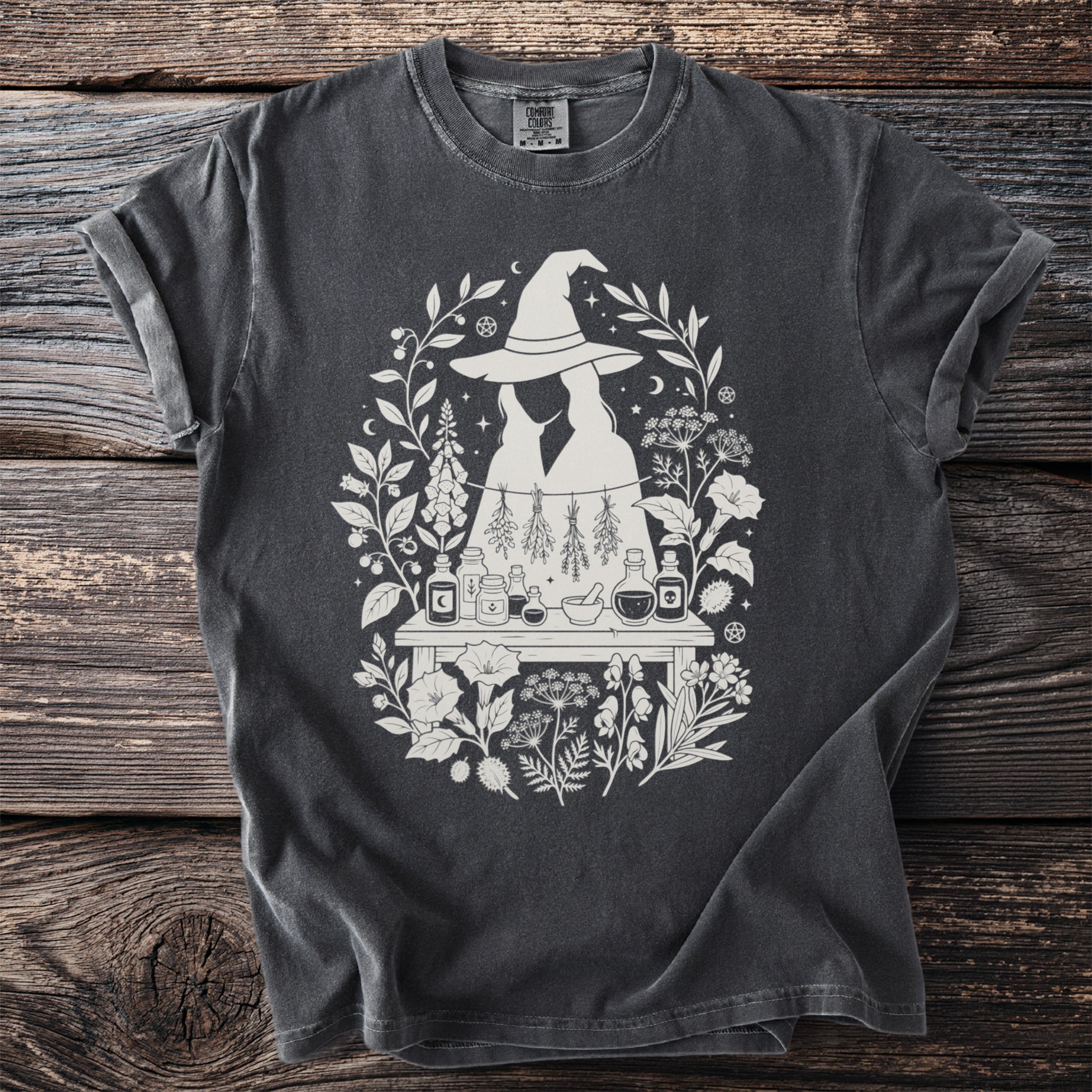 Dark gray t-shirt with white witchy floral design and potion bottles.