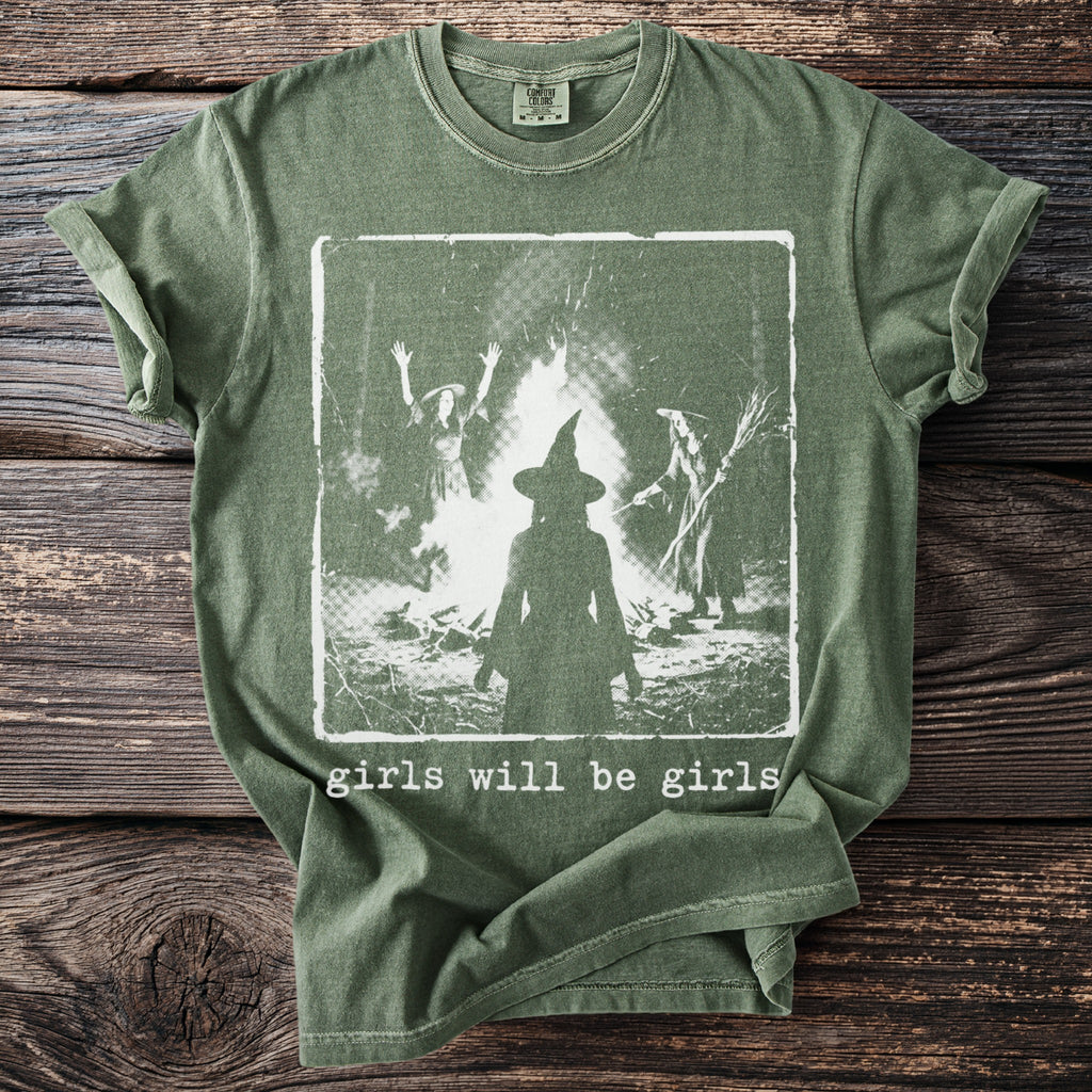 Green t-shirt with graphic of witches around a bonfire and text "girls will be girls".