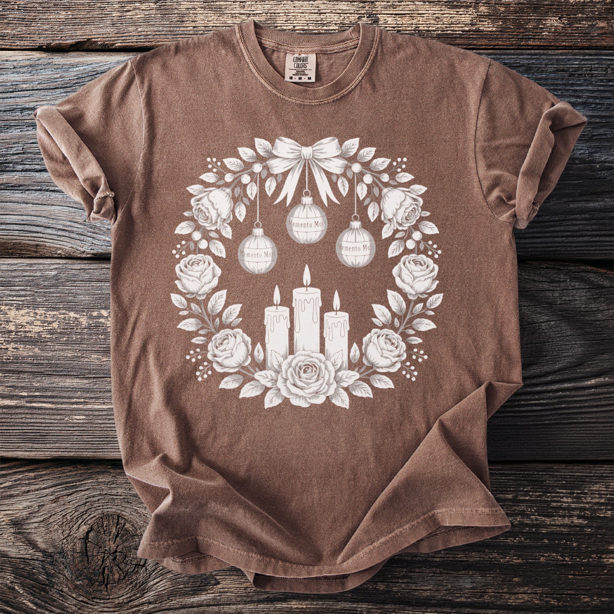 Brown t-shirt with a floral wreath design featuring candles, ornaments, and roses.