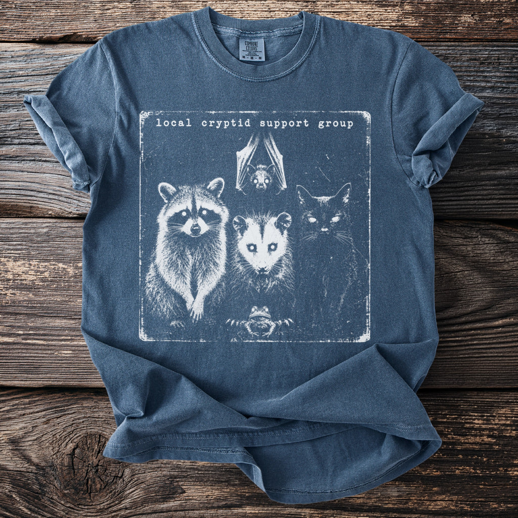Dark blue t-shirt with "local cryptid support group" text and illustrated raccoon, opossum, cat, bat, and frog.