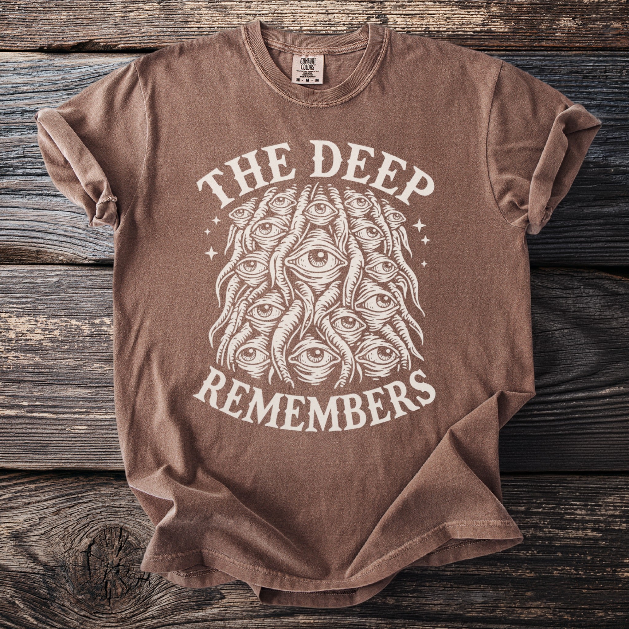 Brown t-shirt with white graphic text "THE DEEP REMEMBERS" and all-seeing eye design.