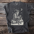 Pepper gray t-shirt with a cream folk-cut print: Krampus sits on a snowy log reading a small book by the light of one candle.
