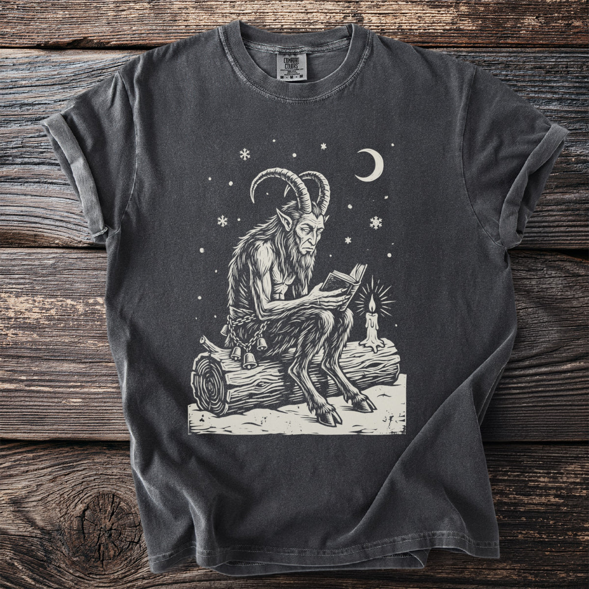 Pepper gray t-shirt with a cream folk-cut print: Krampus sits on a snowy log reading a small book by the light of one candle.