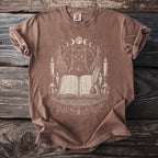 Brown t-shirt with mystical cat, open book, candles, and moon phases design.