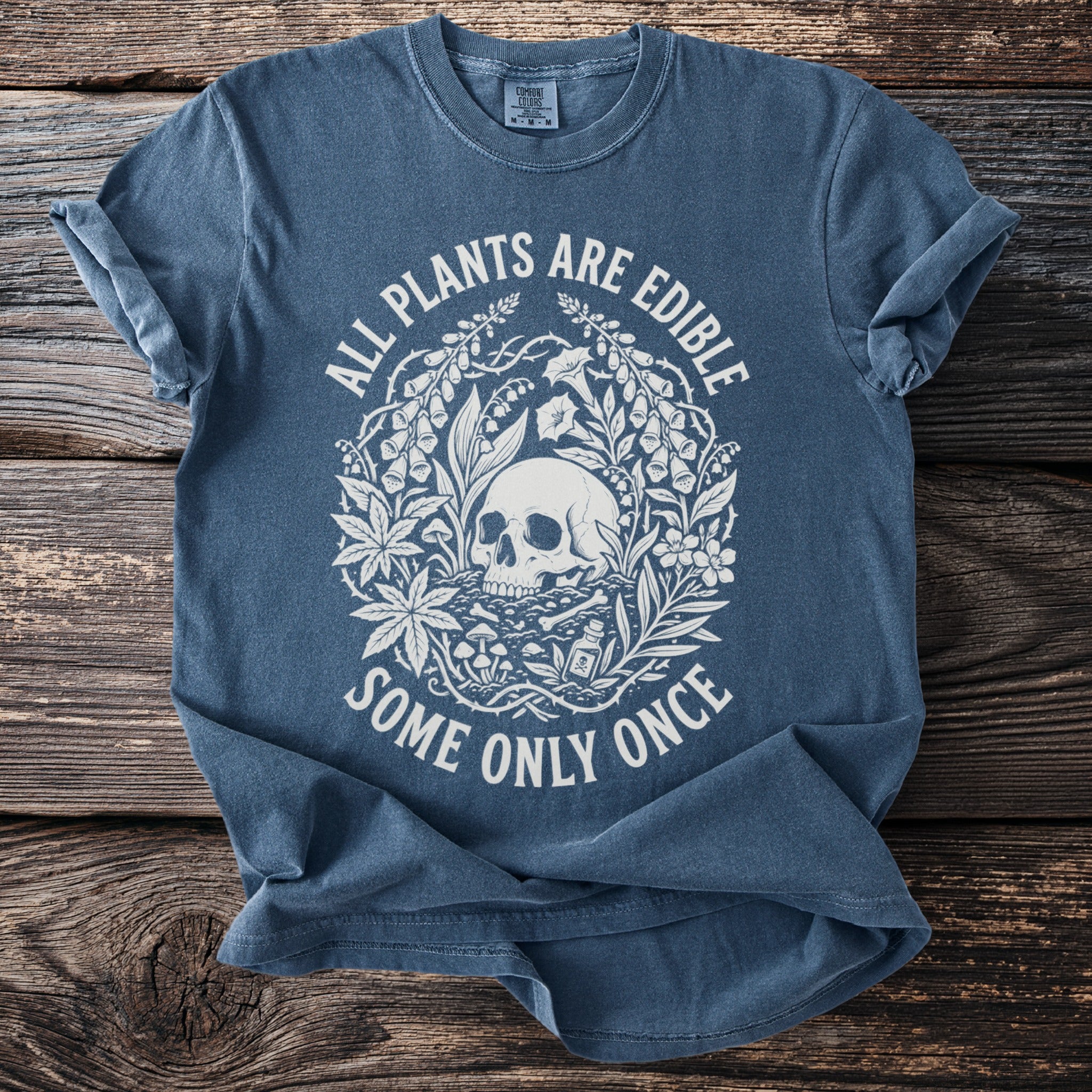 Blue t-shirt with a skull, plants, mushrooms, bones, and drug bottle design and text.