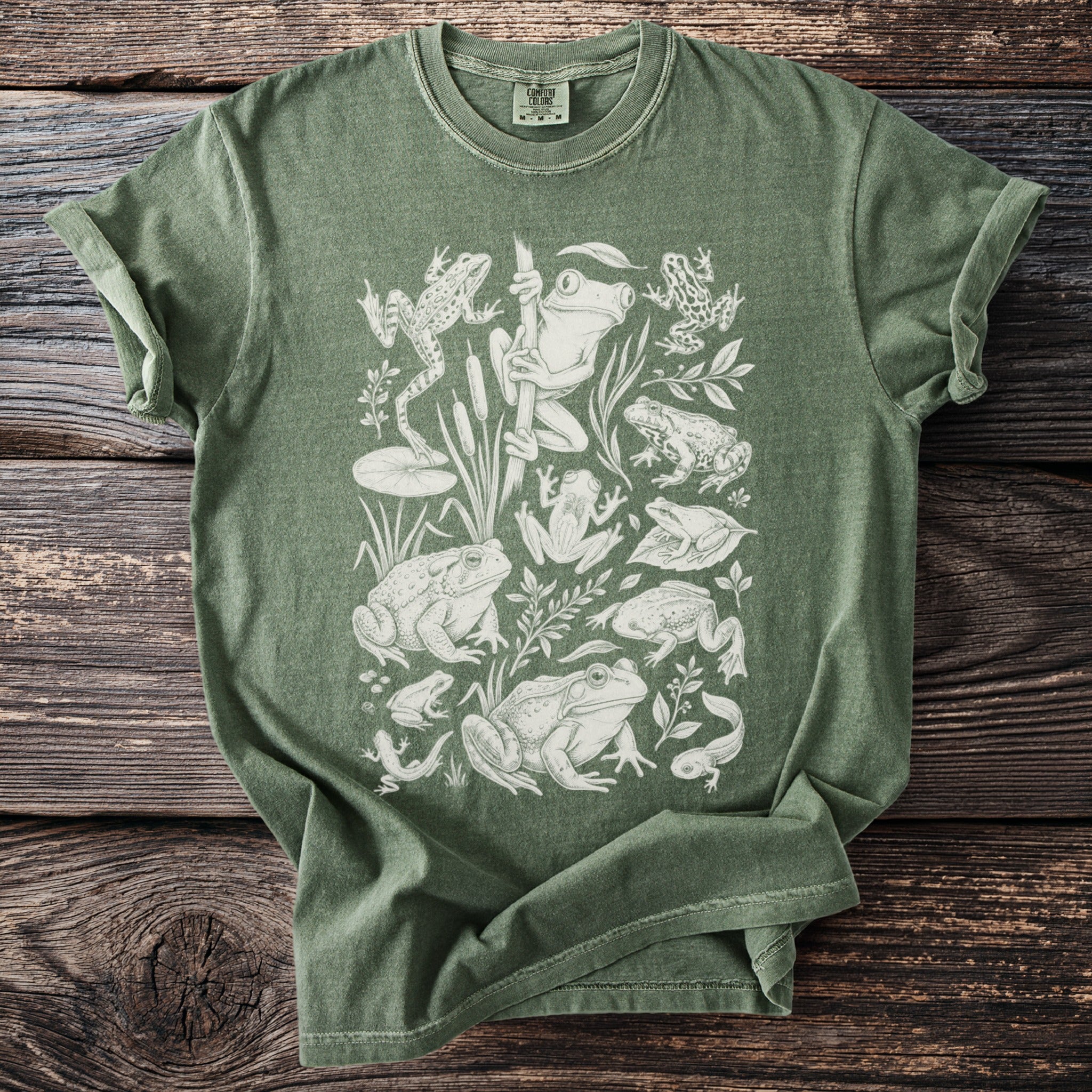 Green t-shirt with white line drawing of various frogs and tadpoles.