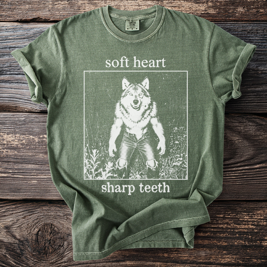 Green t-shirt with white graphic of a wolf standing on hind legs, text "soft heart sharp teeth".