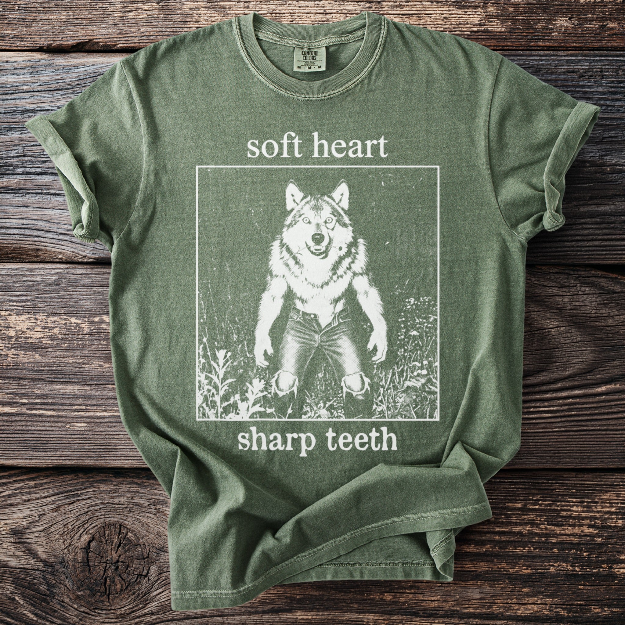 Green t-shirt with white graphic of a wolf standing on hind legs, text "soft heart sharp teeth".