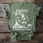 Green t-shirt with Bigfoot by campfire, text says bigfoot grabbed my weiner.