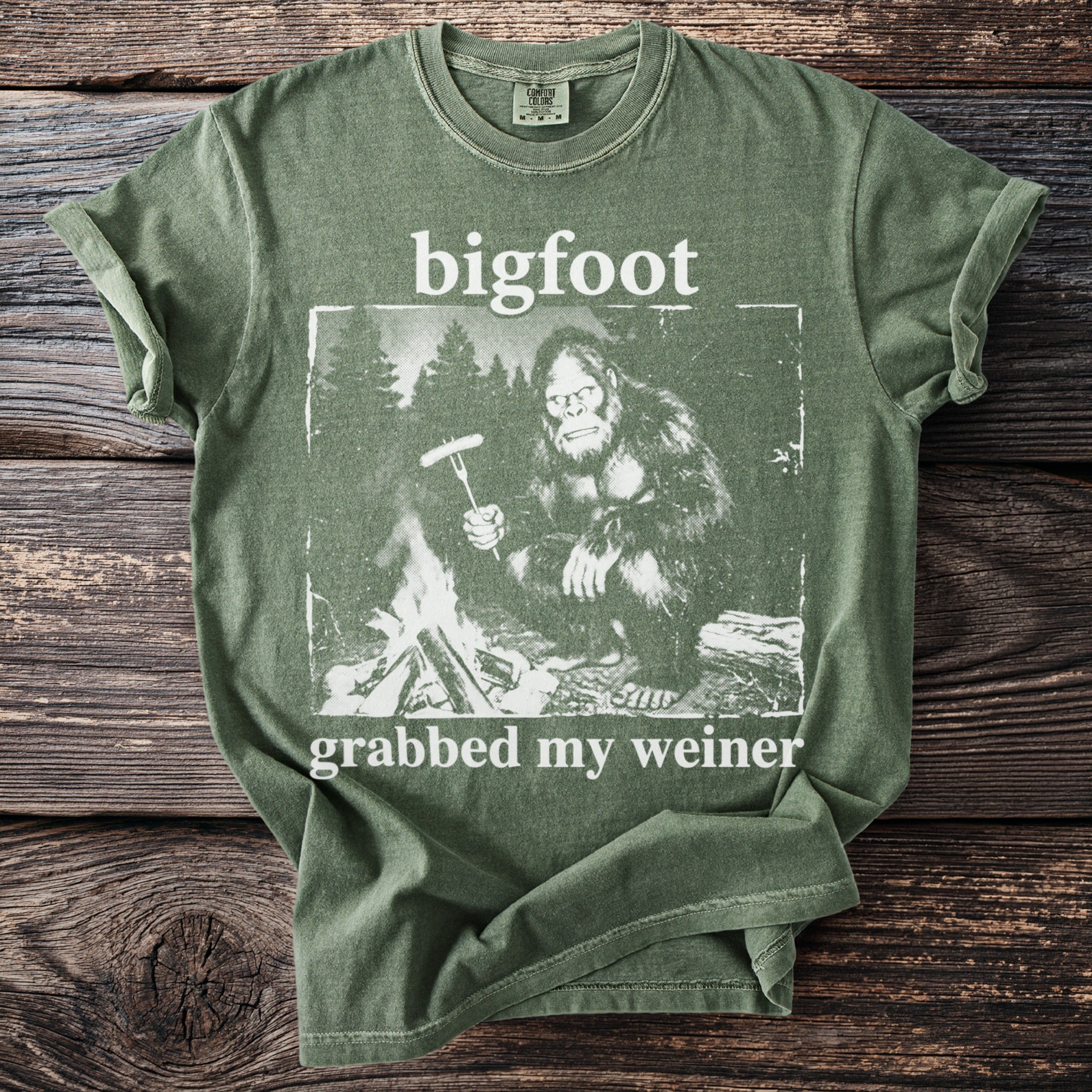 Green t-shirt with Bigfoot by campfire, text says bigfoot grabbed my weiner.